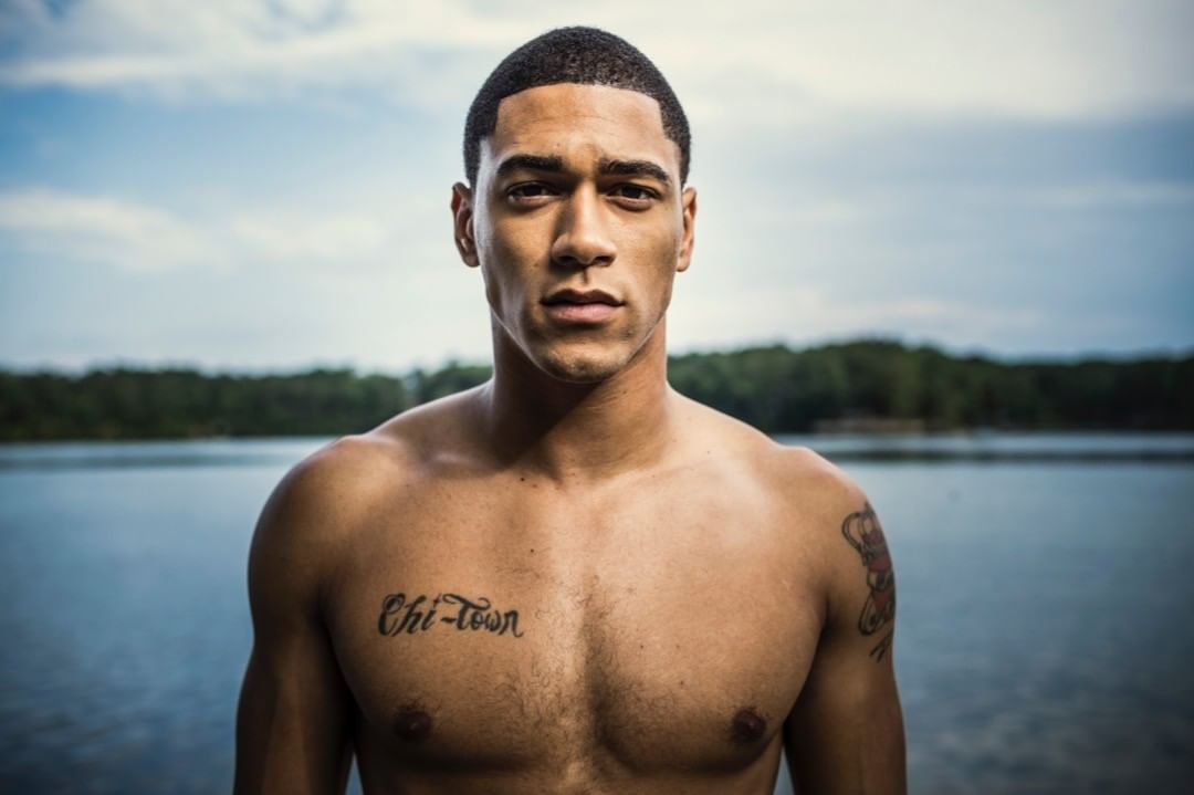 Portrait of shirtless Black man with short hair and chest tattoo posing outdoors near water by Pat Molnar