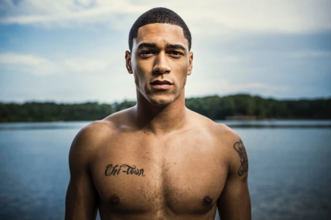 Portrait of shirtless Black man with short hair and chest tattoo posing outdoors near water by Pat Molnar
