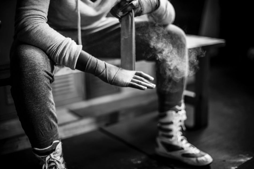 Monochrome shot of a person sitting on a bench, wrapping hands with athletic tape with a cloud of powder in the air.