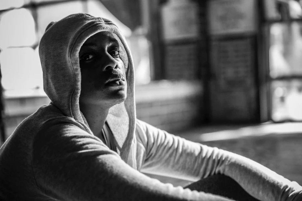 Monochrome portrait of a young adult looking up while wearing a hooded sweatshirt, shot indoors with soft natural light.