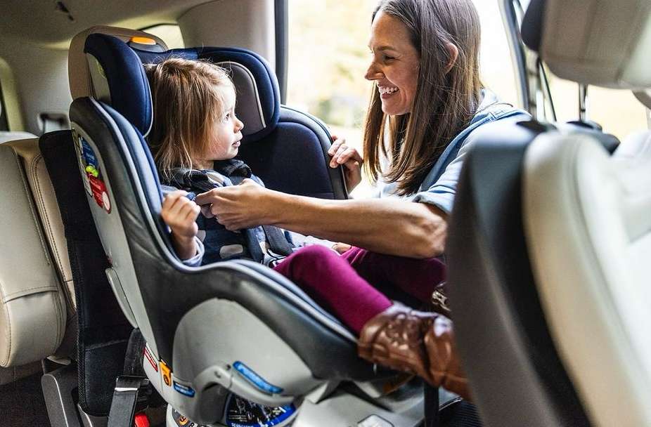 Toddler sits in a car seat in the back of a car as an adult fastens the straps. Family and car safety concept. Child safety in vehicles.