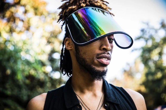 Black man wearing futuristic iridescent visor and dark sleeveless top photographed by Pat Molnar