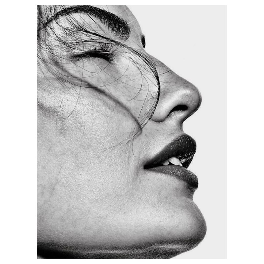 Close-up studio portrait of a woman with closed eyes and dramatic lighting, face angled up against a white backdrop.