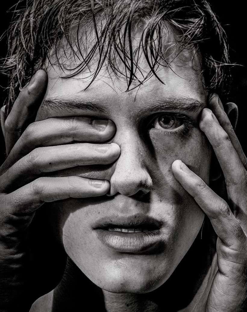 Close-up black and white portrait of a young man with wet hair framing his face with his hands.