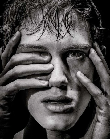 Close-up black and white portrait of a young man with wet hair framing his face with his hands.