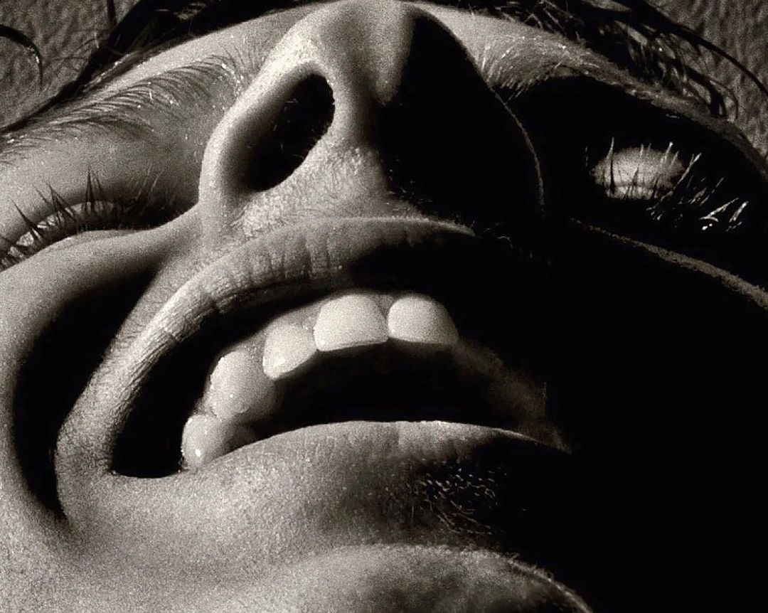 Close-up studio shot in monochrome capturing an upward view of a person's open mouth, nose, and eyelashes, creating stark contrasts.