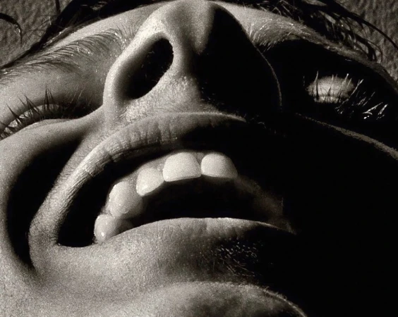 Close-up studio shot in monochrome capturing an upward view of a person's open mouth, nose, and eyelashes, creating stark contrasts.