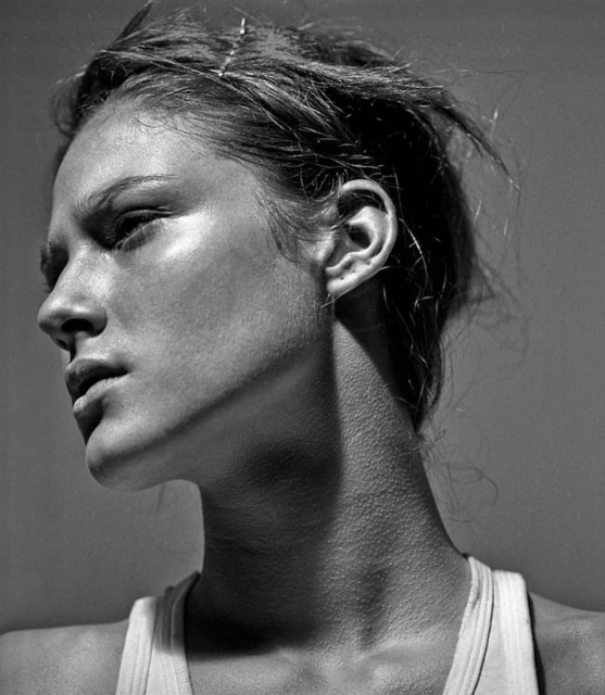 Monochrome portrait of a woman in profile, showing her face, neck, and shoulder against a neutral background, with natural light.