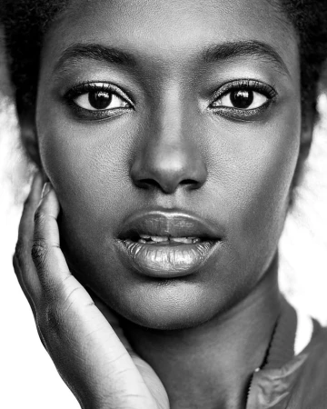 Close-up monochrome portrait of a Black woman with her hand resting against her face against a white background