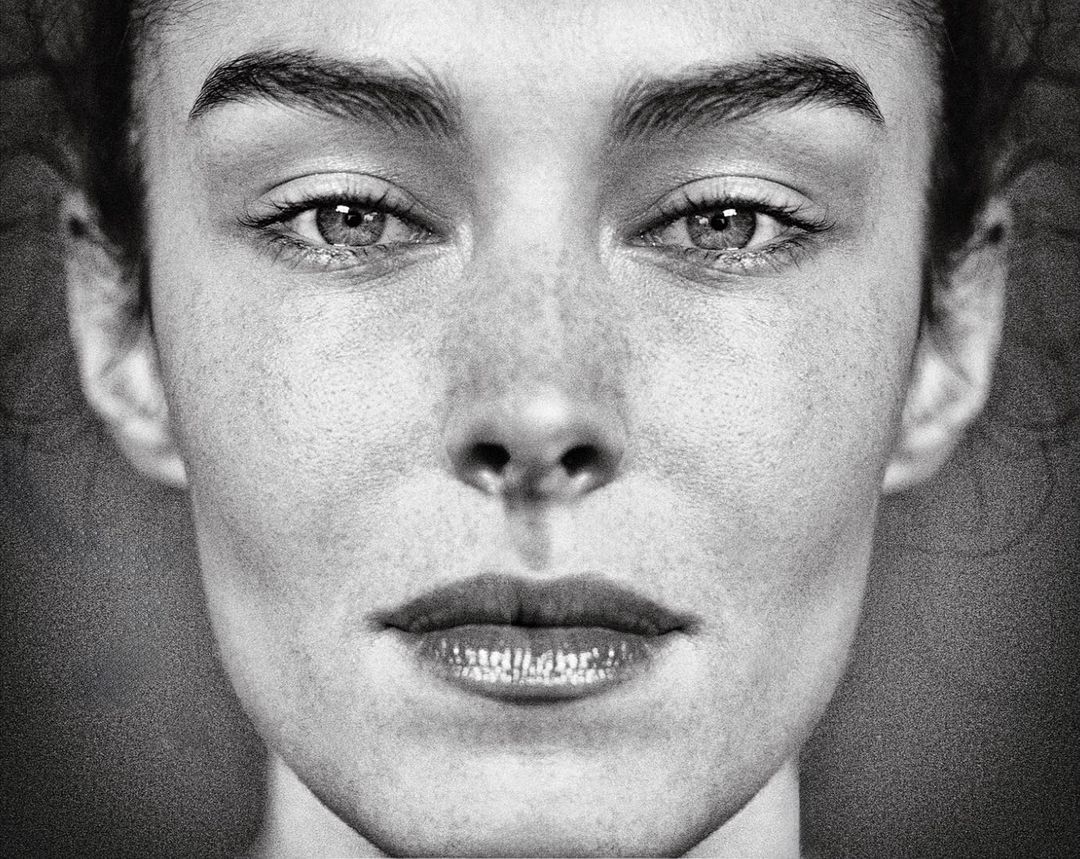 Black and white close-up portrait of a woman with freckles, featuring a symmetrical composition and natural lighting.