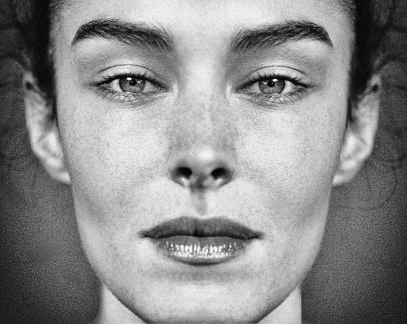 Black and white close-up portrait of a woman with freckles, featuring a symmetrical composition and natural lighting.