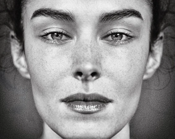 Black and white close-up portrait of a woman with freckles, featuring a symmetrical composition and natural lighting.