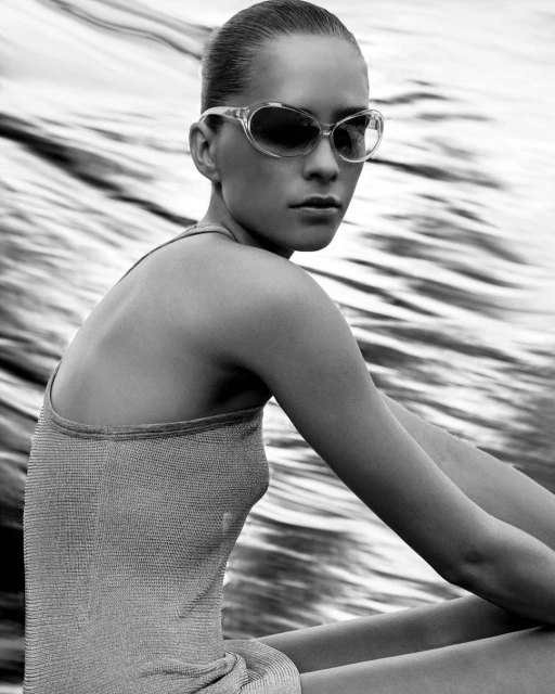 Monochrome portrait of a woman in sunglasses and a tight top, posing against a blurry background, creating a vintage fashion vibe.