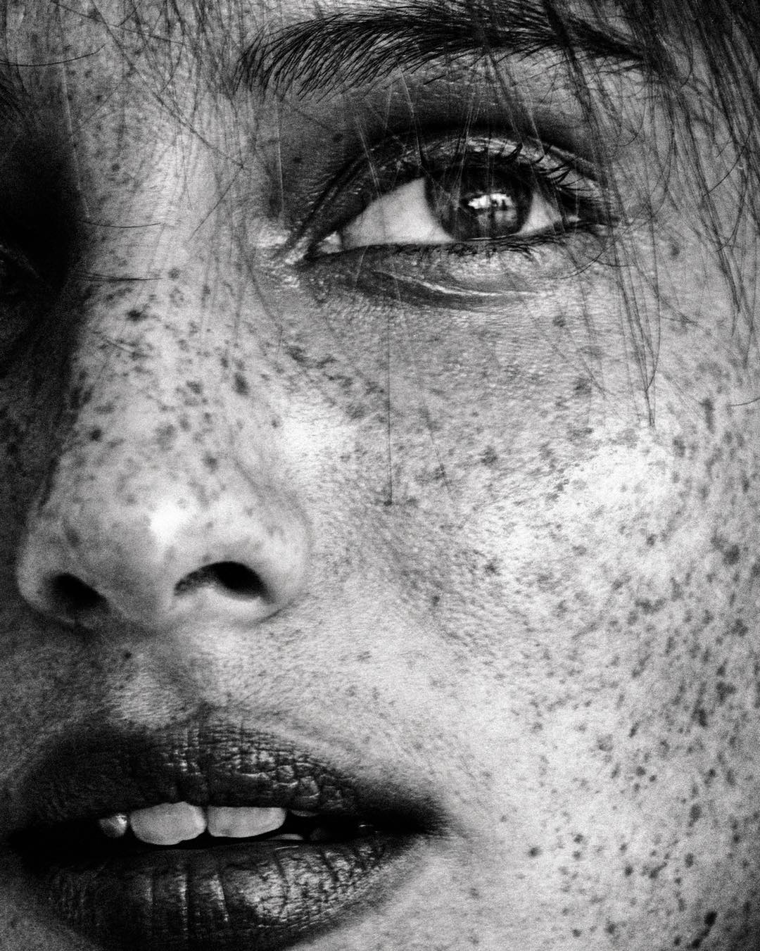 Monochrome extreme close-up of an adult woman's face, focusing on the right eye, nose, and mouth, emphasizing skin freckles in a beauty shot.