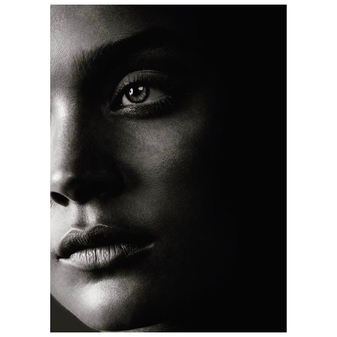 Close-up of a dark-skinned adult female's face in a portrait showing an eye, nose, and lips, with a black background.