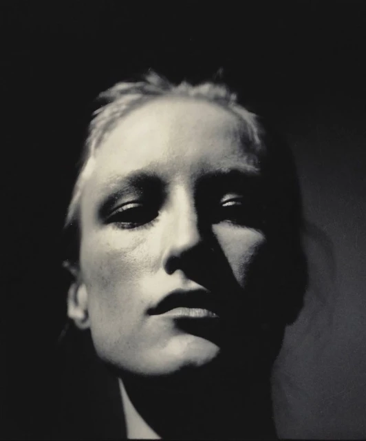 Monochromatic portrait of a woman with dark hair in a low-key lighting setup, face angled slightly down creating dramatic shadows.