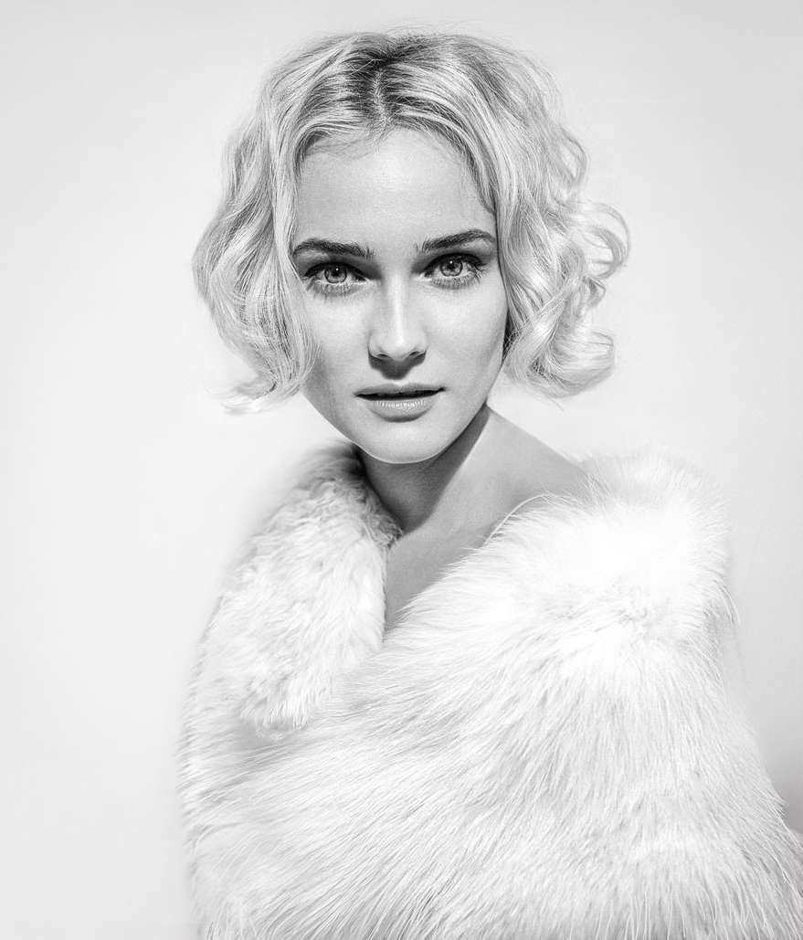 Black and white portrait of a blond woman wearing a fur stole, close-up studio shot with shallow depth of field and soft lighting.