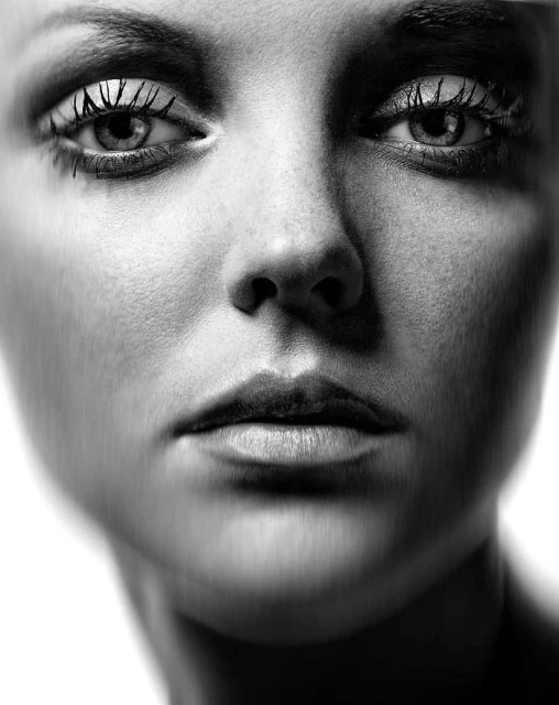 Monochrome close-up portrait of a woman's face showcasing detailed skin texture, eyes with lashes, and soft lighting.