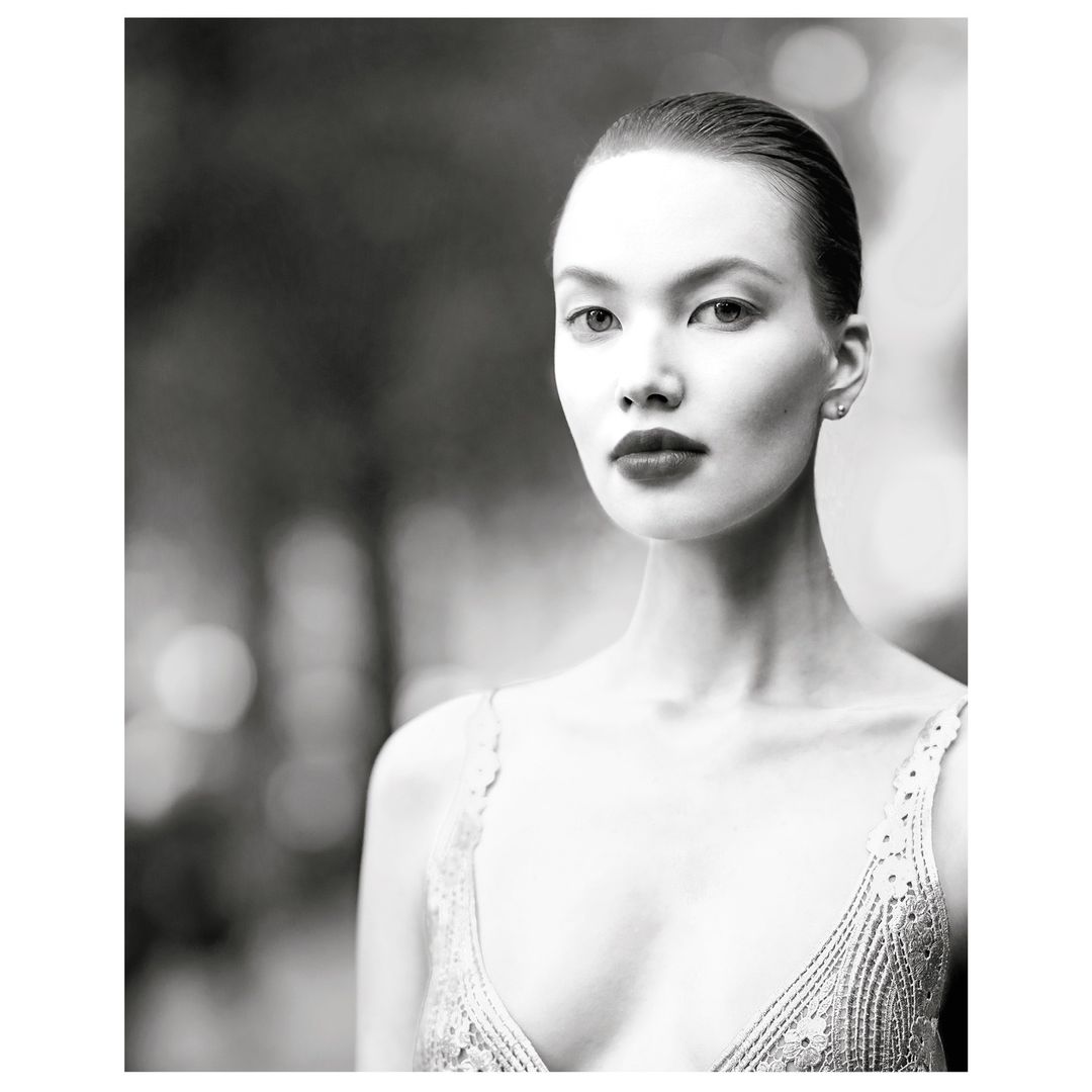 Portrait of an adult female with an elegant lace top against a blurred outdoor background, black and white photography, elegant look.