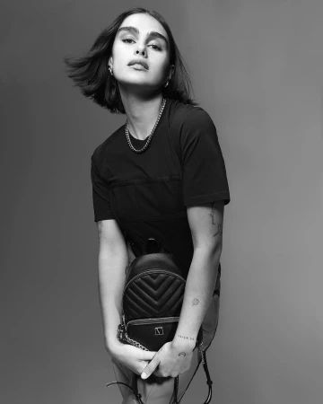 Portrait of a woman with dark hair holding a quilted black backpack, shot in black and white by Patric Shaw in Paris.