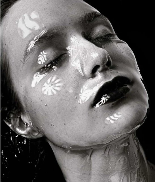Monochrome close-up of a woman's face with wet skin and black lipstick, featuring patterned light reflections and a dark background.
