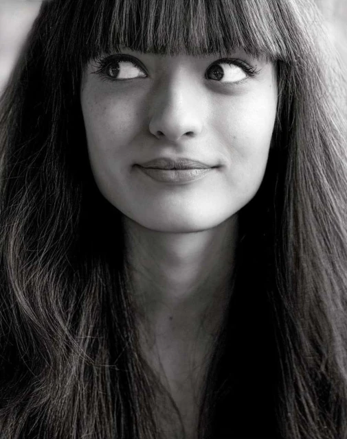 Black and white portrait of a young woman with bangs looking to the side, showcasing her long hair and distinct facial features.