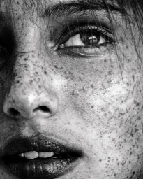 Extreme close-up portrait of a woman face in monochrome, showing detailed skin texture and prominent freckles.