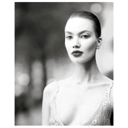 Monochrome portrait of a woman with slicked back hair and dark lips wearing a patterned strap top against a soft blurred background