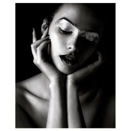 Close-up portrait of a woman with metallic silver eye makeup and dark lips, framing her face with both hands against a black background.