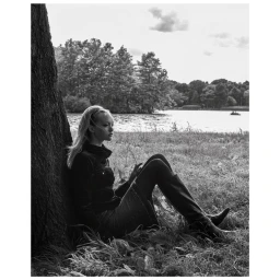 Monochrome portrait of a young woman sitting against a large tree trunk by a lake, photographed by Patric Shaw.