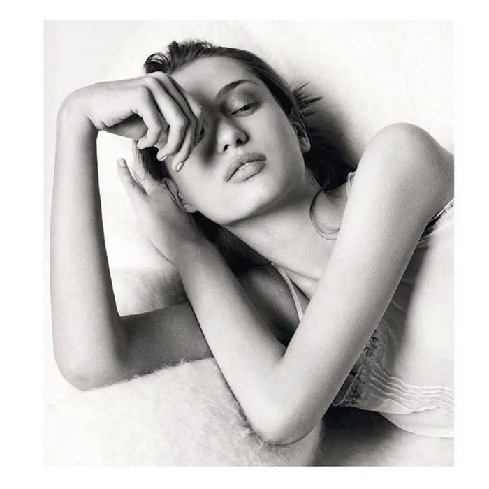 Black and white portrait of a woman reclining with her hand raised near her face against a plain light background