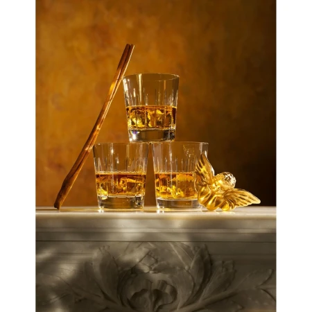 Three whiskey glasses stacked with liquid and ice, plus gold cherub and cinnamon sticks, on a marble surface against a tan background.