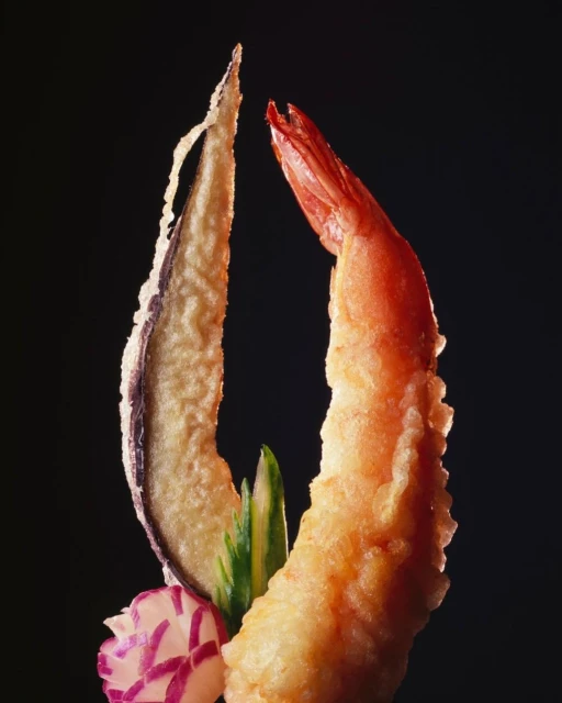 Close-up of shrimp and vegetable tempura on a black backdrop, showcasing the textures and colors of Japanese cuisine.