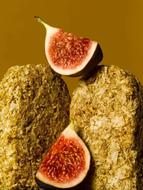 Still life photo of two fig slices placed on top of two grainy rocks, set against a solid brown background. Food and beverage.