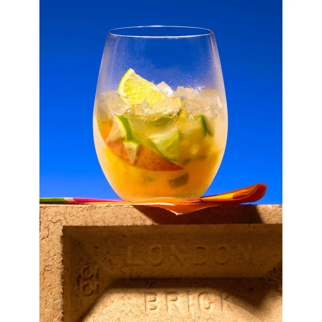 Cocktail in a glass with lime and ice sitting atop a brick with 'London Brick' text, set against a blue background, creating a refreshing and vibrant image.