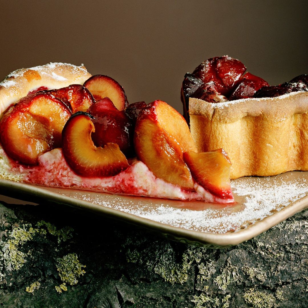 Close-up of plum tarts on a rustic surface, showcasing fresh plums, golden crust, and a dusting of powdered sugar for a delectable dessert.