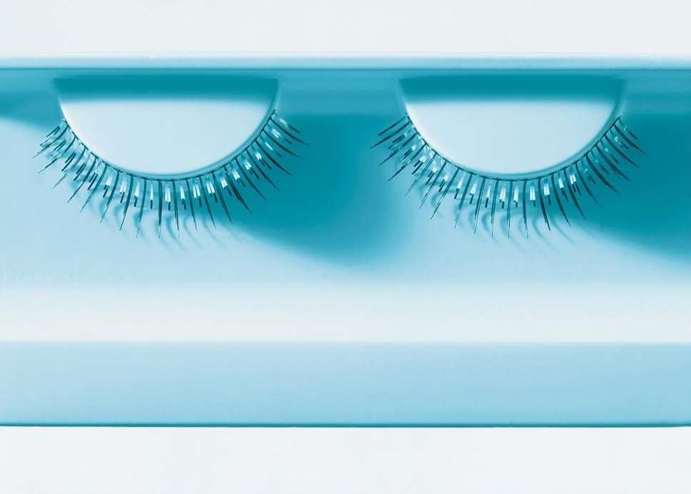 Close-up of a pair of false eyelashes in a blue plastic case, displayed against a white surface, beauty accessory, minimal.