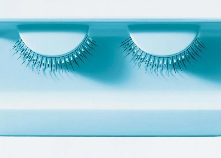 Close-up of a pair of false eyelashes in a blue plastic case, displayed against a white surface, beauty accessory, minimal.