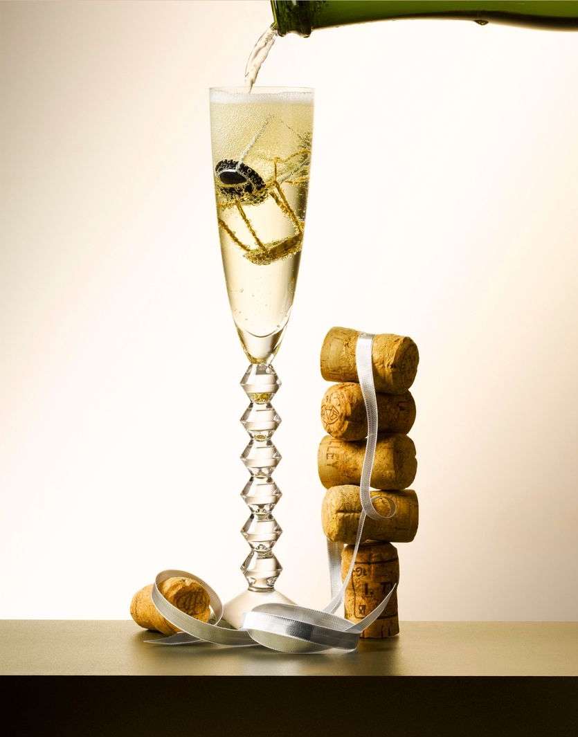 Champagne glass being filled with bubbly liquid, with corks and ribbon, set against a soft, gradient background, creating a celebratory still life.