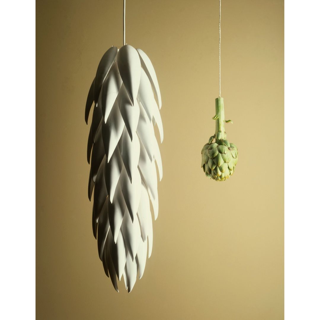 Artichoke-shaped pendant lamp alongside an actual artichoke hanging against a tan background in a studio setting. Interior design.