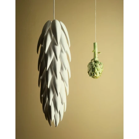 Artichoke-shaped pendant lamp alongside an actual artichoke hanging against a tan background in a studio setting. Interior design.
