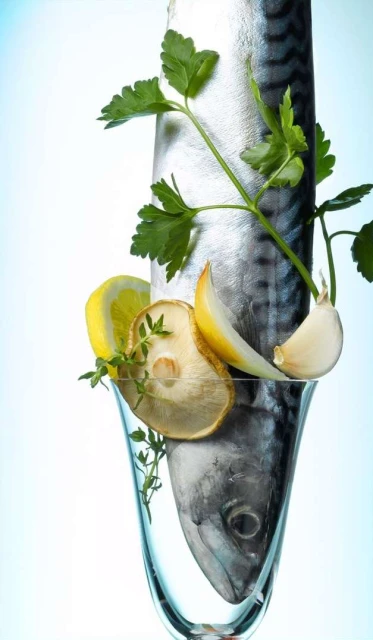 Mackerel fish in a stemmed glass with lemon wedges, garlic, and parsley sprigs, creating a fresh and culinary-inspired still life.