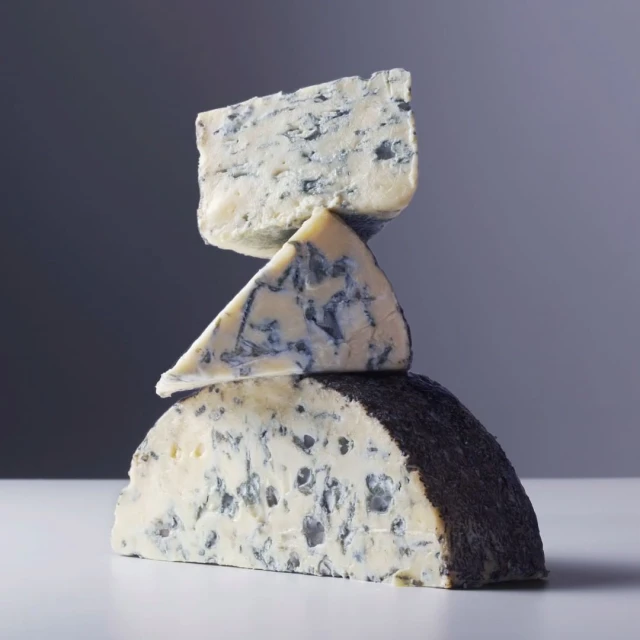 Stack of three wedges of blue cheese with white and blue marbling against a gradient grey background in a still life food photograph.