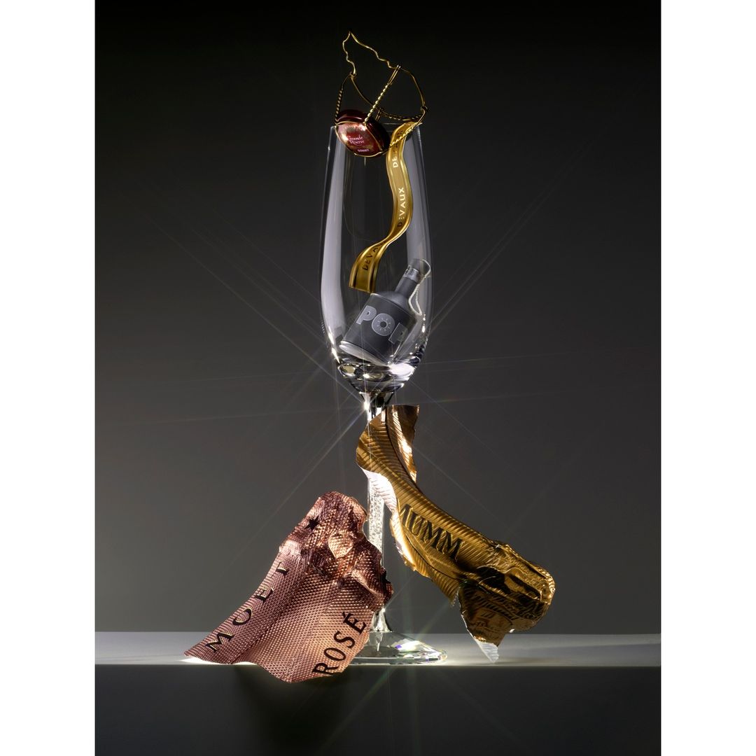 Still life shot of a champagne flute with packaging elements around it, set against a gray background with studio lighting.