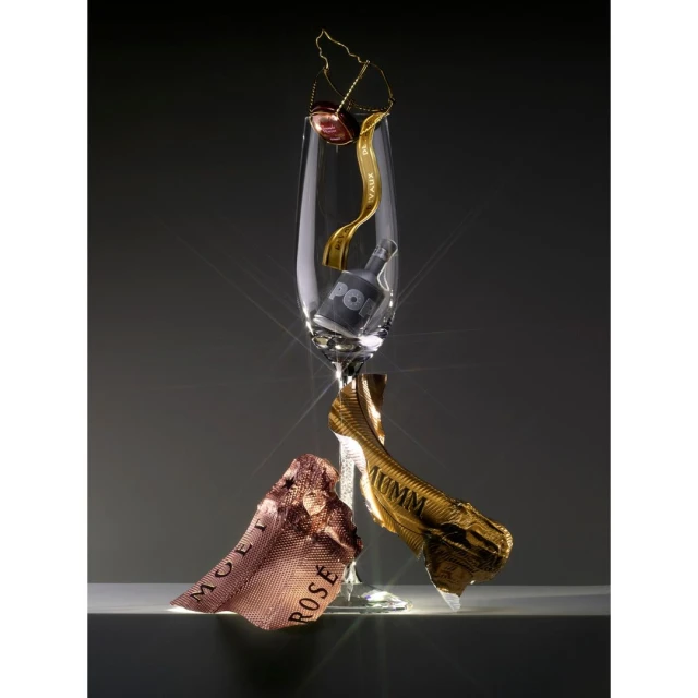Still life shot of a champagne flute with packaging elements around it, set against a gray background with studio lighting.