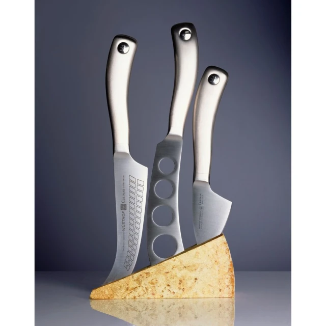 Studio shot of three stainless steel knives in a cheese wedge knife block, studio lighting, kitchenware, and food and beverage focus.