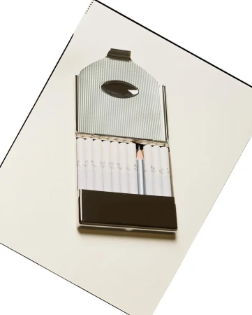 Open silver cigarette case with white cigarettes and a single white pencil on a white surface, angled shot, indoor studio.