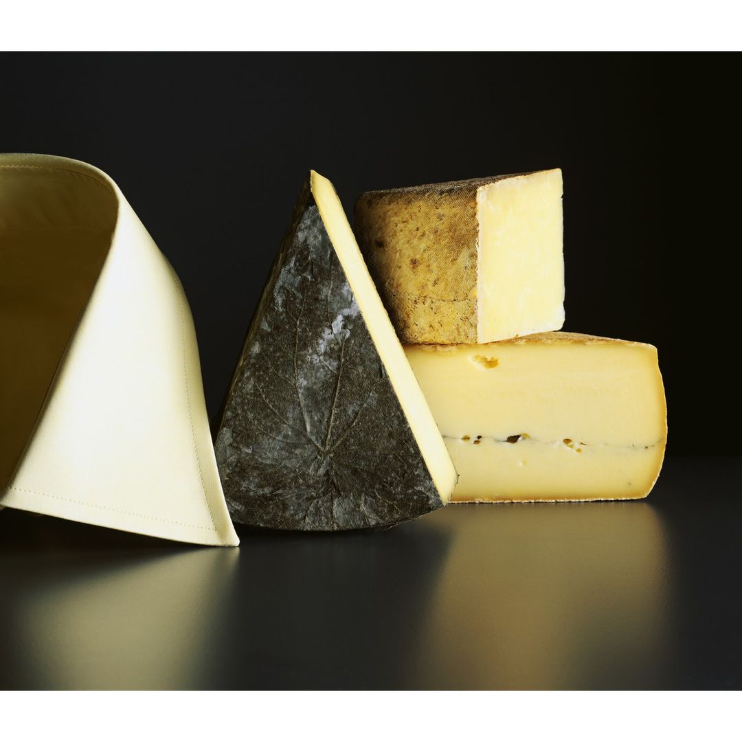 Assortment of cheeses arranged on a reflective black surface with a black background, with a folded white textile on the left.