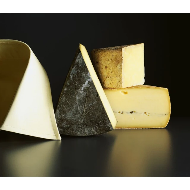 Assortment of cheeses arranged on a reflective black surface with a black background, with a folded white textile on the left.