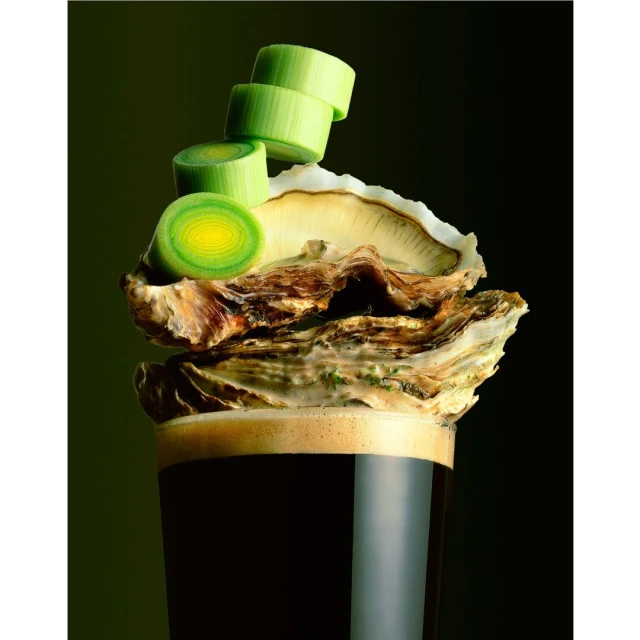 Dark stout topped with a raw oyster shell and fresh scallion garnish against a dark green backdrop, creating a visually striking food still life.